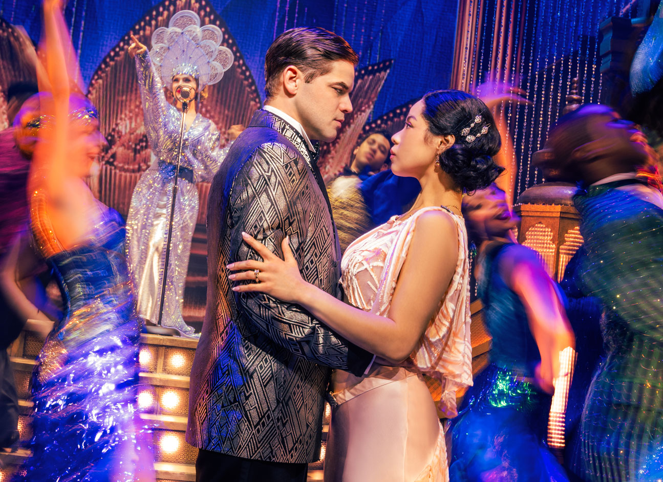 Jeremy Jordan and Eva Noblezada as Jay Gatsby and Daisy Buchanan embrace on a dance floor, at an extravagant party, looking into each other's eyes very seriously